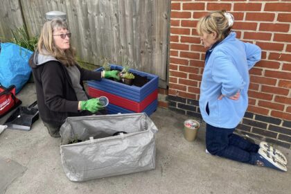 Two ladies planting a red and blue planter on a thornton heath pavement